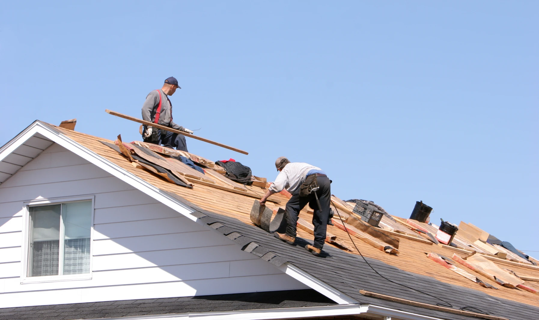 Two men working on the roof of a house, with one of them holding a wooden stick